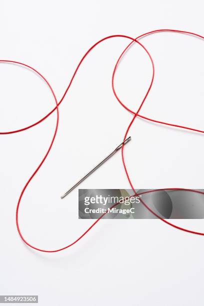 red tangled thread passing through a sewing needle - thread sewing item stock-fotos und bilder