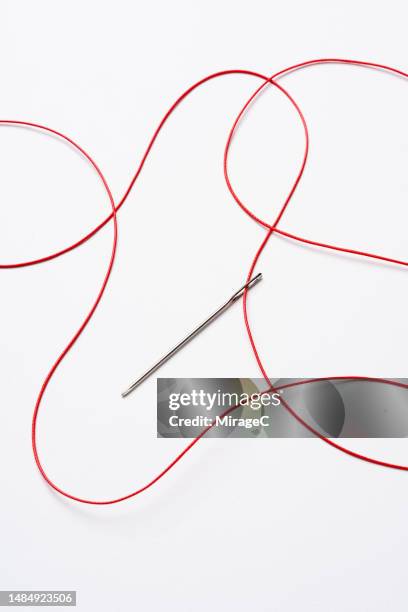 red tangled thread passing through a sewing needle - rode draad stockfoto's en -beelden