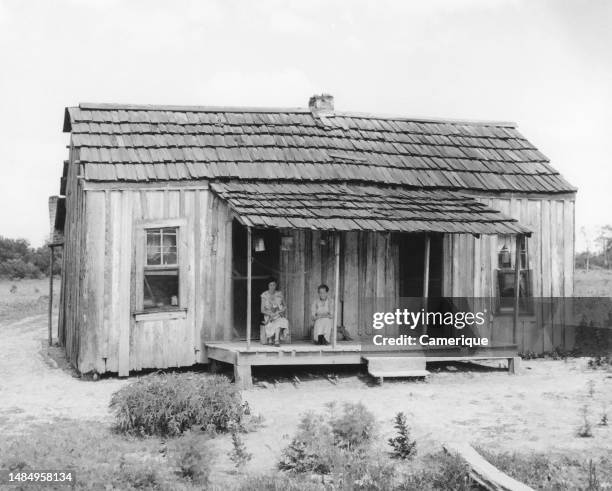 Exterior view of a sharecropper's home in Arkansas with two people sitting on the front porch, dated 9/20/1945