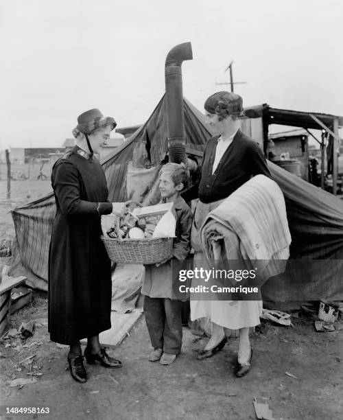 Older woman giving a basket of cheer to a boy and his mother in a what appears to be a camp.