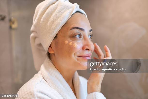 woman applying cream to her face i̇n the bathroom - applying cream stock pictures, royalty-free photos & images