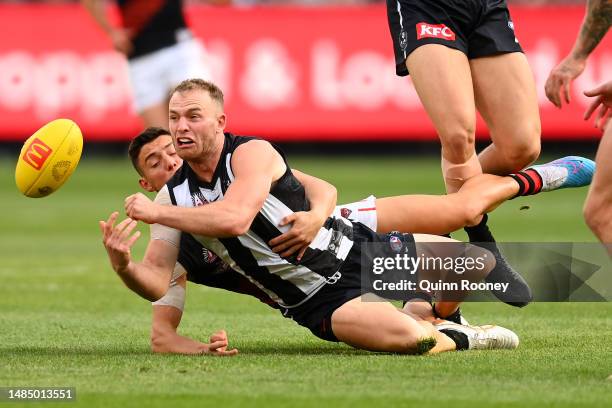 Tom Mitchell of the Magpies handballs whilst being tackled by Jye Caldwell of the Bombers during the round six AFL match between Collingwood Magpies...