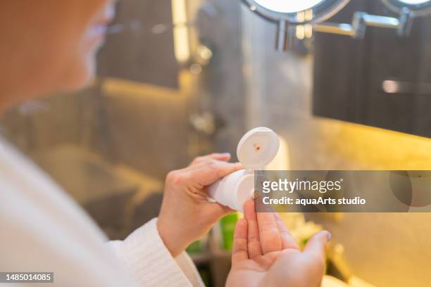 woman squeezing cream i̇nto her hand i̇n a cream tube - robe tube stock pictures, royalty-free photos & images