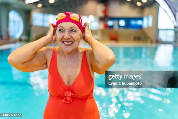 mujer mayor activa mirando hacia otro lado y sonriendo después de nadar en la piscina cubierta - female bathing suits fotografías e imágenes de stock