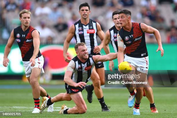 Jye Caldwell of the Bombers handballs whilst being tackled by Tom Mitchell of the Magpies during the round six AFL match between Collingwood Magpies...