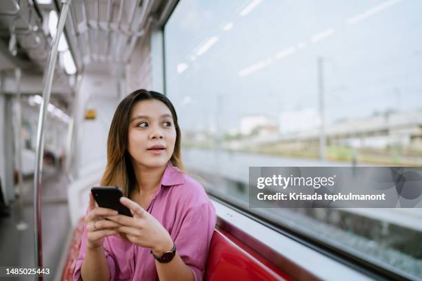 asian woman looking at view from inside rapid transit while traveling to work outside office. - commuter benefits stock pictures, royalty-free photos & images