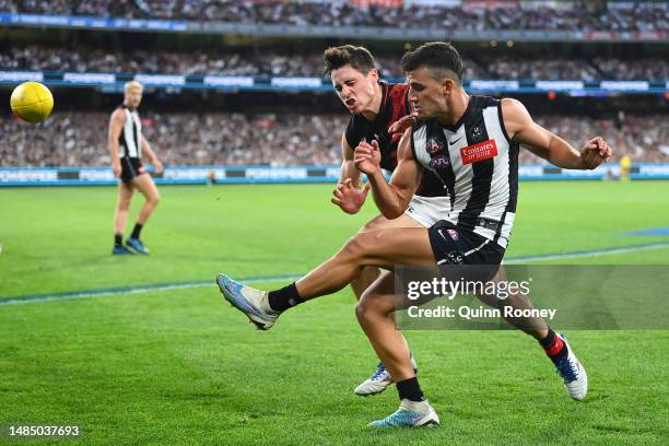 Nick Daicos of the Magpies kicks whilst being tackled by Jake Kelly of the Bombers during the round six AFL match between Collingwood Magpies and...