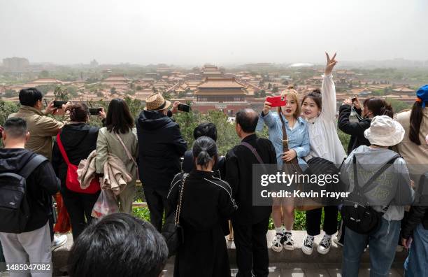 Visitors take photos as the Forbidden City and Palace Museum can be seen shrouded in dust as they visit Jingshan Park during a sandstorm on April 25,...