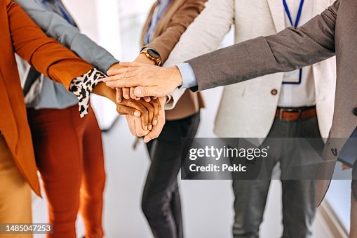 Close up shot of unrecognisable business people stacking hands together at the office hallway