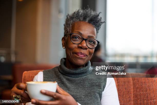 senior adult black female enjoying her morning coffee at a cafe on a gloomy morning in london - rich people stock pictures, royalty-free photos & images