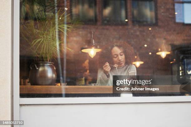 young woman using cell phone and eating in cafe - view-through-restaurant-window stock pictures, royalty-free photos & images