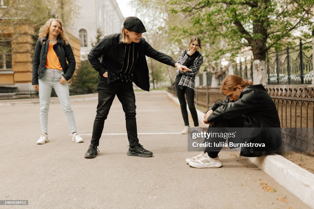 A group of students laughing and pointing at a sad nerd sitting on a curb in the school yard