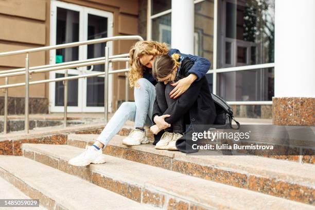 unrecognizable female students sitting on the steps of the school, a friend supporting a frustrated disappointed and sad girl - domestic violence victim stock pictures, royalty-free photos & images
