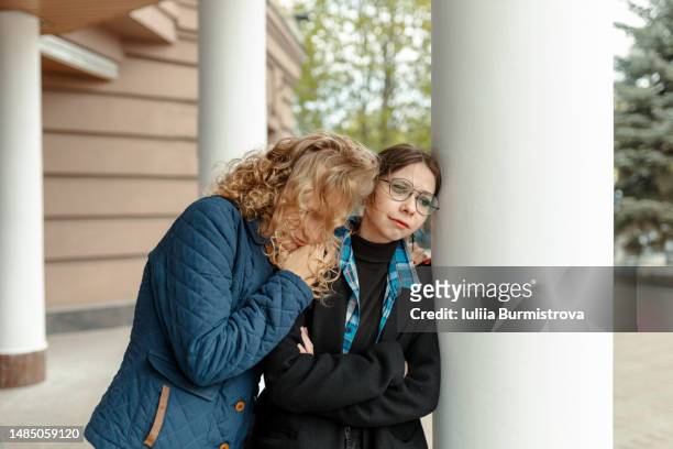 two sad upset depressed female students who are being abused by aggressive behavior of classmates - toxic friendship stock pictures, royalty-free photos & images