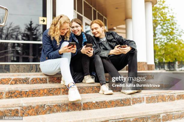 diverse groups of students sitting on the steps of the university having fun and using mobile phones - 3 teenagers mobile outdoors stockfoto's en -beelden