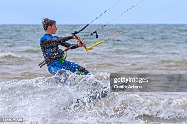 Young kiteboarder. Kitesurfer wearing wetsuit on twintip board kitesurfing on the North Sea.