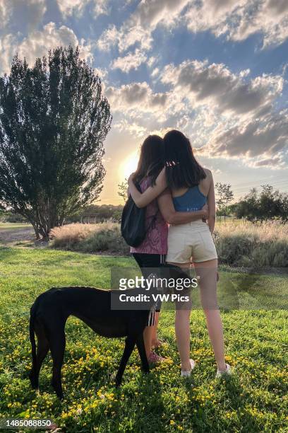 Mother and daughter with dog hugging outdoors.