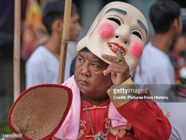 Man lifts his Chinese mask in a procession through the streets of Phuket Town, Phuket Vegetarian Festival . The Vegetarian Festival is a religious...
