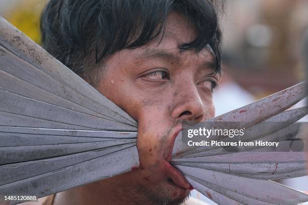 Mah Song or spirit mediums carries multiple blades inserted through his cheek; during the Vegetarian festival in Phuket, Thailand. The Vegetarian...