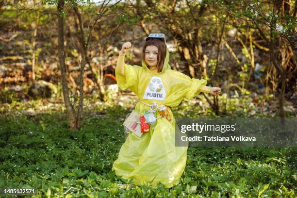 little girl posing in yellow dress made of plastic bag standing in park during summer day - trash bag dress stock pictures, royalty-free photos & images