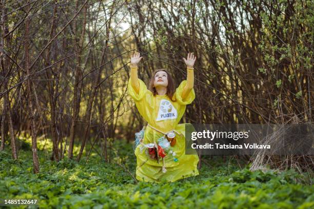 female child wearing plastic and trash found in forest standing with arms raised - trash bag dress stock pictures, royalty-free photos & images