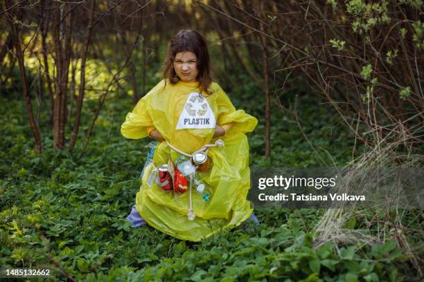 small girl in plastic dress playfully displaying frustration standing in green grass - trash bag dress stock pictures, royalty-free photos & images