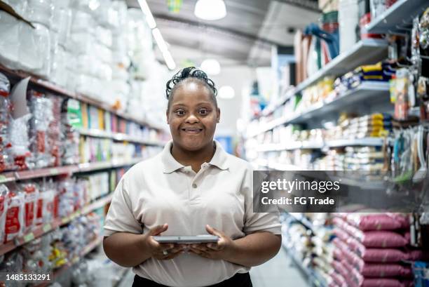 portrait of a young woman with down syndrome working on a digital tablet at the supermarket - down syndrome stock pictures, royalty-free photos & images