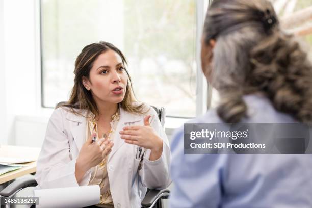 la doctora adulta media hace gestos mientras explica su recomendación al paciente - bata de laboratorio fotografías e imágenes de stock