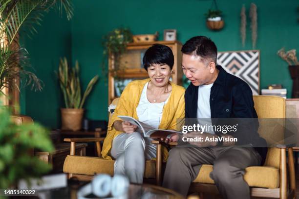 happy senior asian couple sitting on armchair in the living room, enjoying time together, relaxing and reading a travel magazine. elderly and retirement lifestyle - decoração de quarto rapaz imagens e fotografias de stock