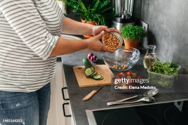 hands of a girl preparing a salad of fresh vegetables and chickpeas. a young woman adds chickpeas to a cucumber, tomato and lettuce salad. healthy eating - chickpea stock pictures, royalty-free photos & images