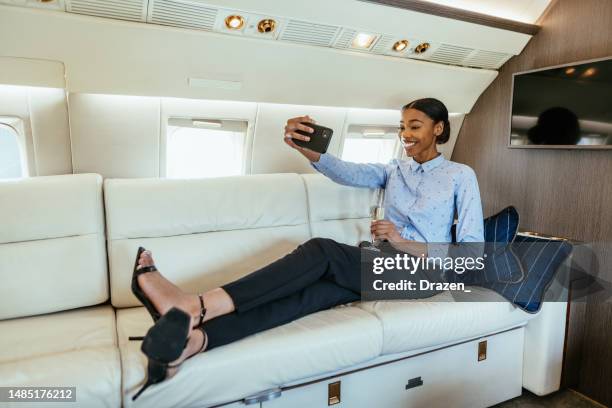 young african businesswoman lying on couch in private airplane and taking selfie - jet lag stockfoto's en -beelden