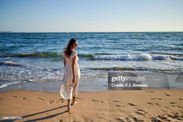 rear view of woman facing the sea at sunset - woman long dress beach stock pictures, royalty-free photos & images