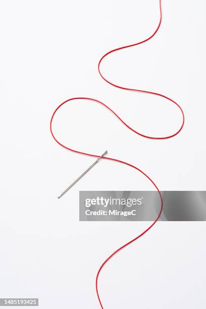red s-shape thread passing through a sewing needle - coser fotografías e imágenes de stock