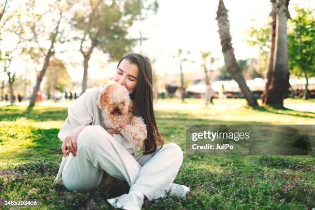 young adult woman with her maltipoo dog walking in public park - lap dog stock pictures, royalty-free photos & images