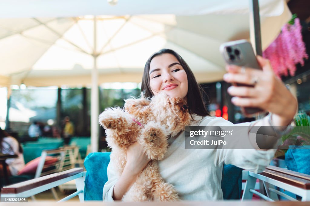 Young adult woman making selfie in cafe with her little dog