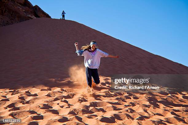 tourists running down red sand dune. - jordan country stock pictures, royalty-free photos & images