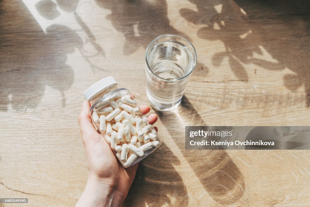 Woman doctor nutritionist hands in white shirt with omega 3, vitamin D capsules with green vegan food. The doctor prescribes a prescription for medicines and vitamins at the clinic