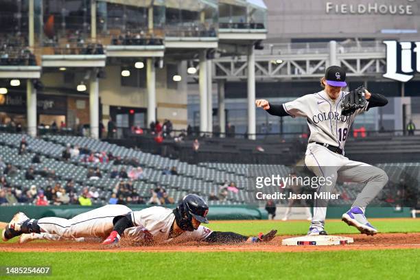 Andres Gimenez of the Cleveland Guardians dives for first as starting pitcher Ryan Feltner of the Colorado Rockies beats him to the tag during the...