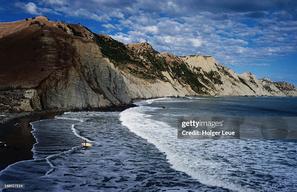 Cliffs along coastline with surfer heading out into waves.