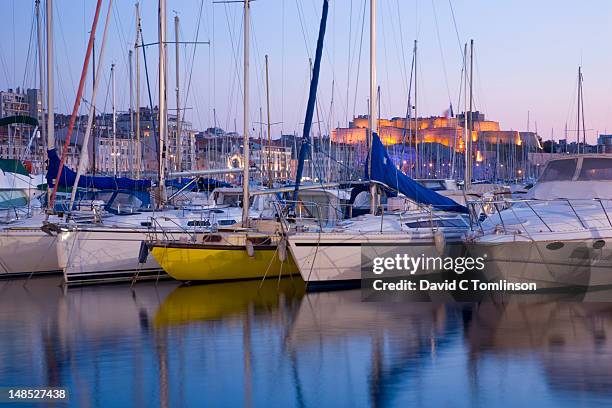 yachts moored in vieux port at dusk with illuminated fort st-nicolas in background. - vieux port stockfoto's en -beelden