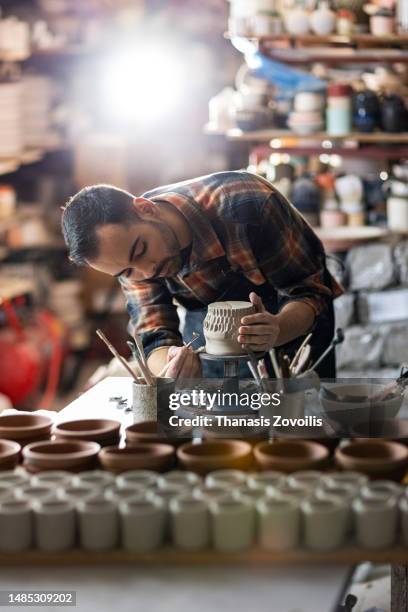 young man potter making pattern on clay mug with special tool in pottery workshop, studio. - sculpture produit artisanal photos et images de collection