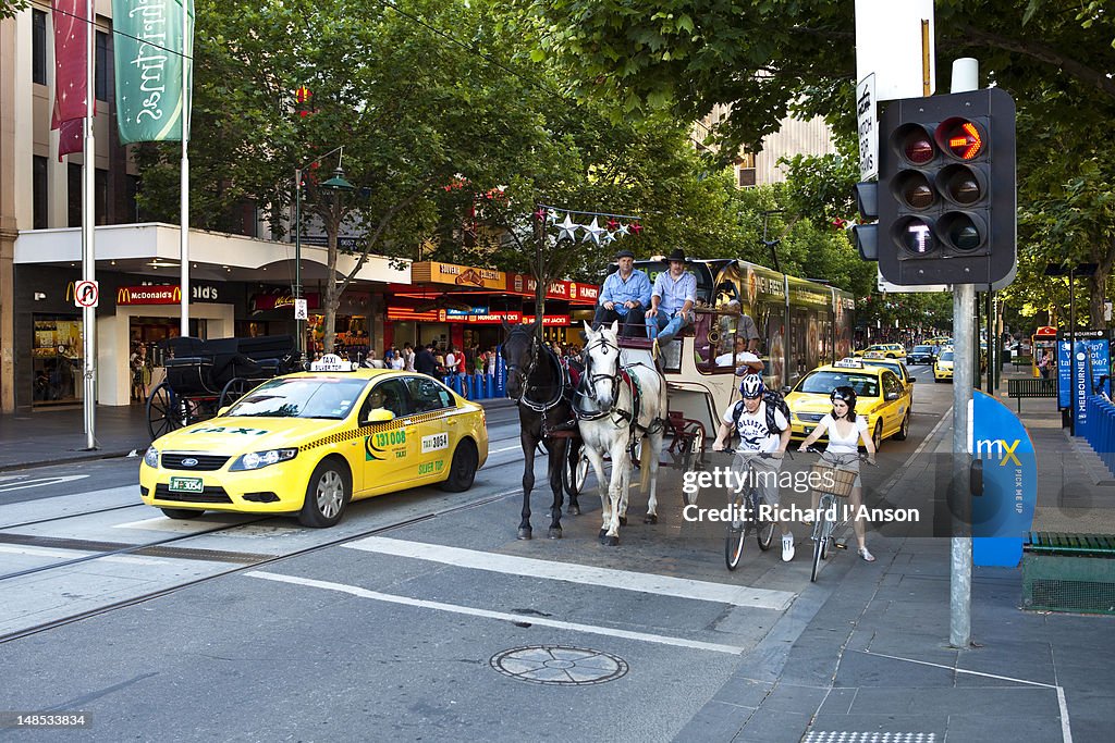 Taxis, horse and cart, cyclists and tram on Swanston Street.