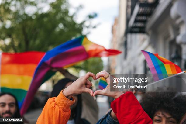des amis genderqueer et non binaires font une forme de cœur contre un drapeau arc-en-ciel - pride événement lgbtqi photos et images de collection