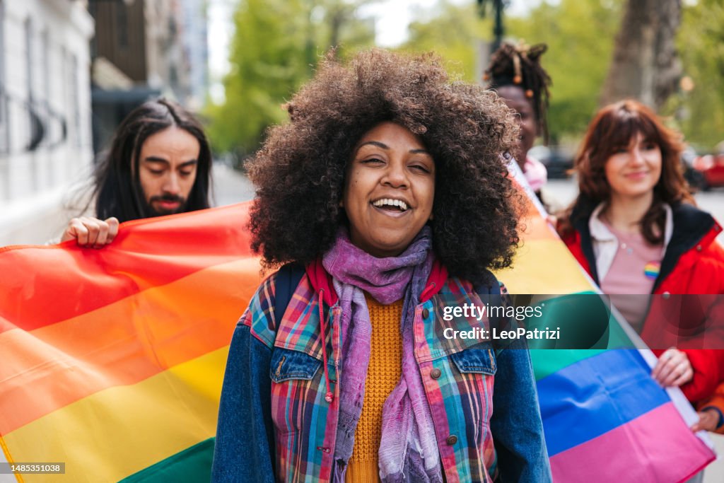 Woman with natural black hair Afro hairstyle posing in front a rainbow flags during a Pride Parade