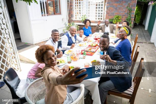 woman holds phone up taking a selfie with multi-generation family having lunch together - large dinner party stock pictures, royalty-free photos & images