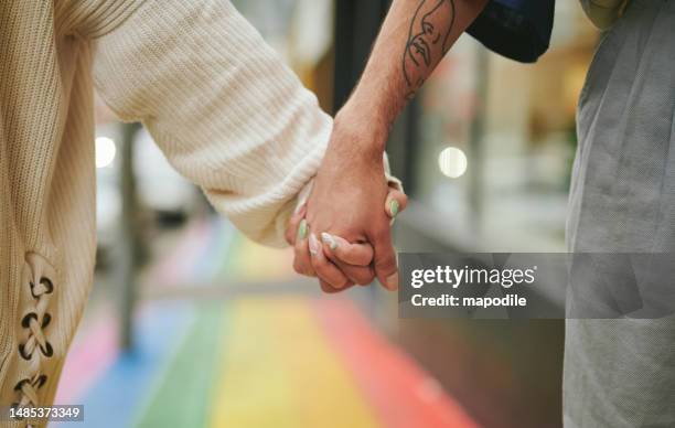 zwei freunde, die sich auf einem bürgersteig in stolzfarben an den händen halten - regenbogenfahne stock-fotos und bilder