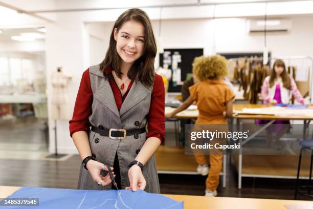 fröhliche modestudentin, die während des kurses stoffe schneidet - technische hochschule stock-fotos und bilder
