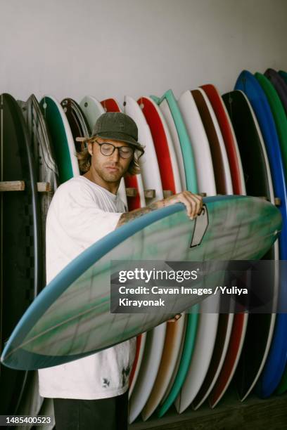 man choosing a surfboard in a surfboard shop - surf store stock pictures, royalty-free photos & images