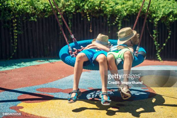 遊び場のブランコで怠惰な一日を楽しむ2人の少年 - 熱波 ストックフォトと画像