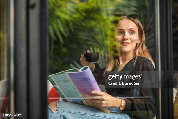 junge frau, die eine zeitschrift liest, junge geschäftsfrau, die aus dem fenster schaut, frau lifestyle - journal stock-fotos und bilder